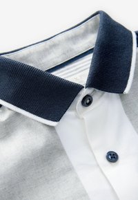 Camisa polo con cuello, que presenta un cuello marino con acentos blancos, un cuerpo gris claro, cierre de botón y un acabado de tejido texturizado.