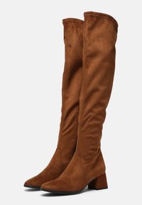 Un par de botas de ante marrón hasta la rodilla con tacones de bloque y punteras puntiagudas, mostradas lado a lado sobre un fondo blanco.