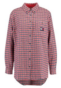 Camicia in flanella a quadri rossa, bianca e blu con maniche lunghe, chiusura con bottoni e tasca sul petto con una toppa logo. Orlo arrotondato.