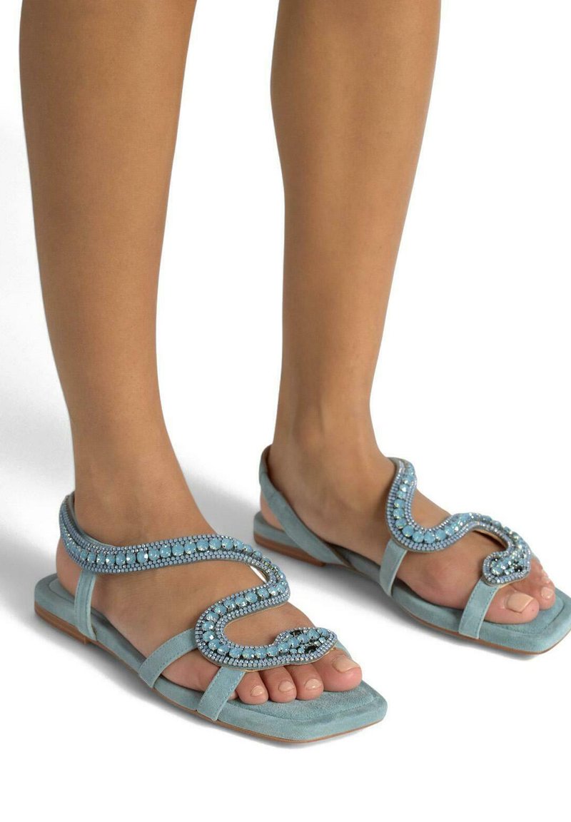 Sandali azzurri chiari in suede con un design decorativo di perline a motivo ondulato. Presentano la punta aperta e una suola piatta.