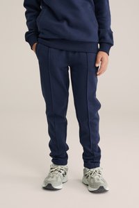 Mörkblåa sweatpants med figursydd design, ribbad linning och sidodetaljer. Kombinerade med ljusgrå sportskor med svarta sulor.