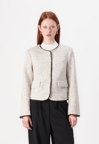 Woven tweed jacket in cream with black accents, round neckline, front pockets, and decorative stitching along the edges.
