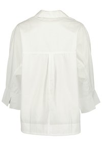 Blusa di cotone bianca con colletto, schiena plissettata e maniche ampie, leggermente accorciate. Presenta spacchi laterali all'orlo per facilitare i movimenti.
