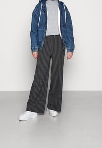 Weite, dunkelgraue Streifenhose, präsentiert mit einer blauen Jeansjacke und einem hellgrauen Oberteil, ergänzt durch weiße Sneakers.