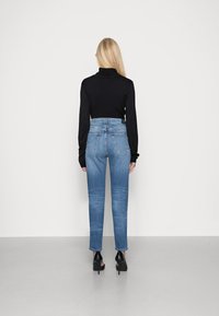 Svart långärmad polotröja parat med midjehöga blå denimjeans. Jeansen har en rak bendesign och bakfickor. Högklackade skor synliga.