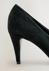 Črne nubuk visoke pete z ostrim nosom in ozkim stiletto peto na svetlo sivi podlagi.