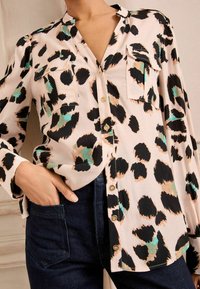 Camicia a maniche lunghe rosa chiaro con stampa leopardata nera e turchese, dotata di apertura frontale con bottoni e due tasche sul petto. Texture morbida.