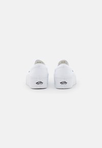 Scarpe slip-on bianche in tela con una suola a piattaforma spessa, dotate di un logo nero sul tallone e una texture liscia.