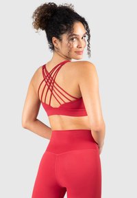 Sujeción deportiva roja con tirantes entrecruzados en la espalda, material elástico y leggings de tiro alto a juego. Textura suave y diseño ajustado al cuerpo.