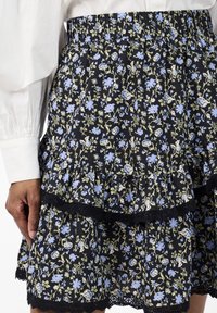 Blomstrete tiered skjørt i svart stoff med blå og grønne blomster mønstre. Elastisk midje med blonder på kanten.