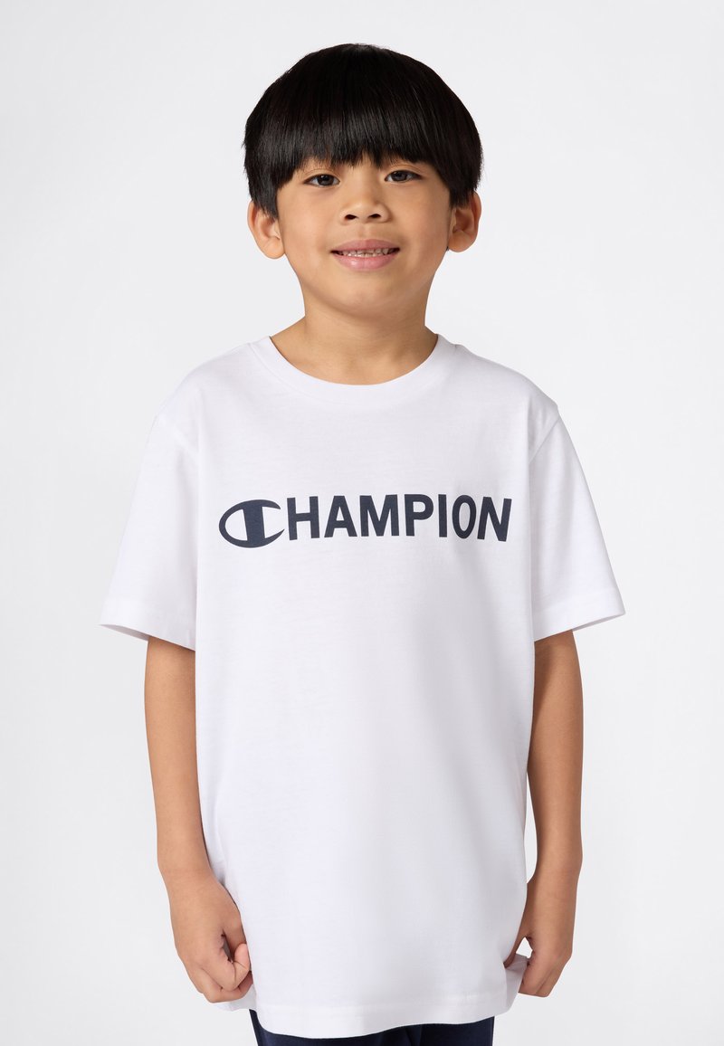 T-shirt en coton blanc avec un grand logo noir "CHAMPION" sur le devant. Manches courtes et col rond.