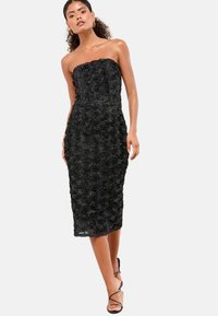 Czarna, strapless, midi sukienka ozdobiona aplikacjami róż, przylegająca do ciała, o gładkiej teksturze i długości do kolan. Całość dopełniają szpilki.
