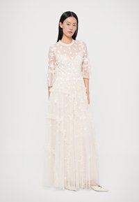 Rochie lungă, de culoare fildeș, dintr-un material transparent, cu broderii florale, mâneci cu volane și detalii stratificate texturate. Lungime până la podea, cu bust modelat.