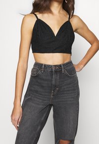 Black lace crop bralette with a deep V-neck, thin straps, and floral pattern. Paired with high-waisted, dark denim jeans featuring distressed details.