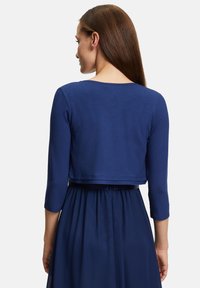 Pull cropped bleu marine avec des manches trois-quarts, texture lisse et encolure arrondie, associé à une jupe fluide bleu marine.