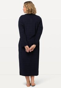 Robe lungo di colore blu navy realizzata in tessuto morbido, con maniche lunghe, taglio dritto e vista posteriore con le mani incrociate dietro.