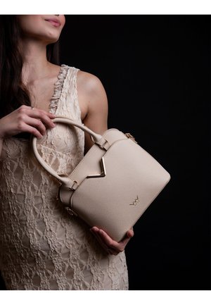 Beige strukturierte Handtasche mit einer strukturierten Oberfläche, ausgestattet mit goldfarbenen Hardwareelementen und einer V-förmigen Akzentuierung auf der Vorderseite.