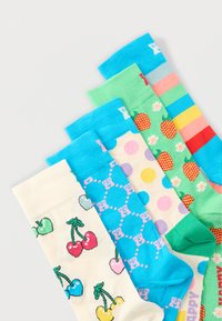 Πέντε πολύχρωμες κάλτσες με μοτίβα όπως κεράσια, pixel art, πουά, φράουλες και ρίγες ουράνιου τόξου, τοποθετημένες σε σχήμα βεντάλιας πάνω σε λευκό φόντο.