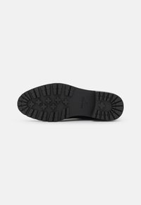 Suela de zapato de goma negra con un patrón de textura. Presenta acentos elevados y letras de la marca; diseño duradero para agarre y estabilidad.