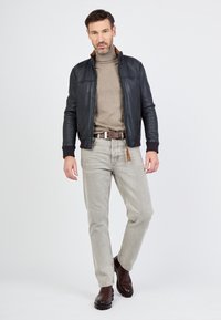 Leren jack in donkerblauw met geribbelde manchetten, gecombineerd met een taupe coltrui, lichtgrijze jeans en bruine schoenen. Eenvoudig, modern ontwerp.