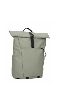 Sac à dos à rabat vert clair en tissu durable, avec une poche zippée à l'avant, des accessoires en noir et un motif géométrique texturé.