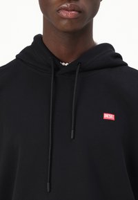 Čierna mikina s kapucňou z bavlny, s nastaviteľnou kapucňou, malým červeným logom "DIESEL" a hladkou textúrou.