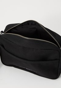 Borsa in tessuto nero con superficie testurizzata, apertura superiore non chiusa con cerniera argentata. Presenta una tasca frontale e un design minimalista.