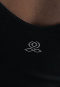 Μαύρο ύφασμα με ένα μικρό λευκό στυλιζαρισμένο λουλουδένιο λογότυπο, τοποθετημένο κοντά στη λαιμόκοψη στο κέντρο.