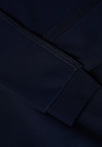 Marineblå sweatshirttype stof med ribkanter, en glat tekstur og en sømdetail for struktur. Nærbillede af materialerne.