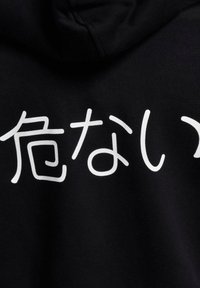 Hoodie noir avec du texte japonais blanc sur le devant. Tissu doux avec une texture lisse. Design décontracté avec une poche frontale et une capuche réglable.