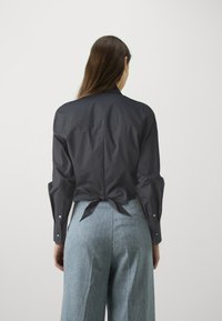 Σκούρο γκρι, εφαρμοστό πουκάμισο με μακριά μανίκια και δέσιμο πίσω. Συνδυασμένο με ανοιχτό μπλε, φαρδιά παντελόνια. Λείο ύφασμα.