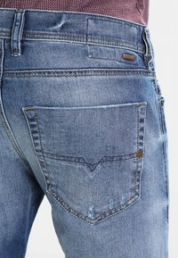 Niebieskie dżinsy z tylną kieszenią ozdobioną subtelnym przeszyciem, metką z logo oraz lekko zużytą fakturą dla swobodnego wyglądu.