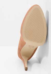 Chaussure à talon haut beige à bout pointu avec semelle texturée, vue de la semelle sur fond blanc en coin.