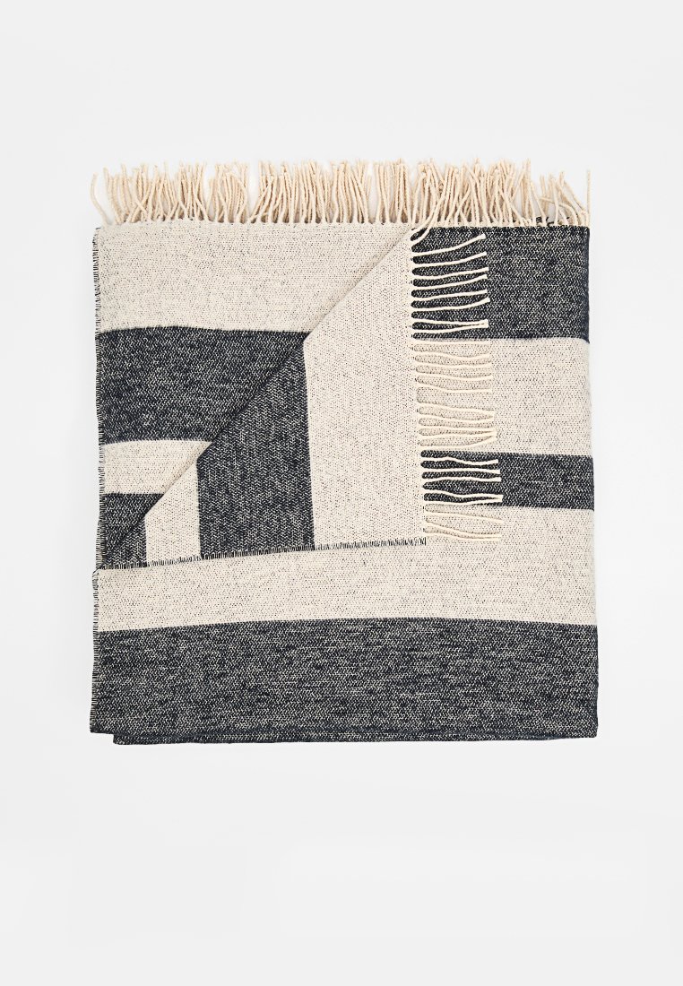 Gewebte Decke mit einem gestreiften Muster in Creme und Dunkelgrau. Abgeschlossen mit langen Fransen an zwei Kanten. Weiche Textur, rechteckige Form.