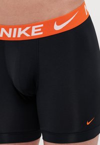 Fekete boxer alsónemű, élénk narancssárga rugalmas derékkal, rajta a "NIKE" logóval és egy kis narancssárga Swoosh motívummal a bal alsó oldalon.