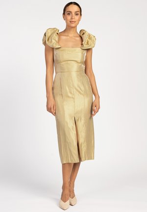 Gold satin dress with structured puff sleeves, square neckline, and front slit. Smooth texture, fitted silhouette, knee-length design, pair of nude heels.