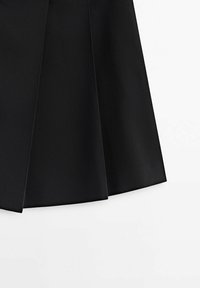 Panneau de tissu noir plissé avec des plis marqués sur fond blanc, mettant en valeur la structure et la texture du vêtement.