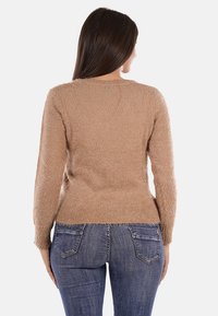 Pullover beige morbido con maniche lunghe, scollatura rotonda e un piccolo dettaglio decorativo sul retro. Abbinato a jeans in denim blu.
