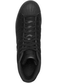 Svart idrottssko med en texturerad gummitåhette, slät läderöverdel och framträdande snörningsdesign. Har tre randiga detaljer.