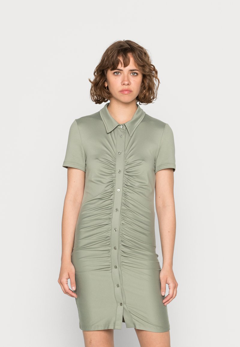 Vestido de manga curta e colarinho em tecido verde suave. Apresenta franzido vertical e botões frontais. Ajustado ao corpo, com uma bainha até ao joelho.