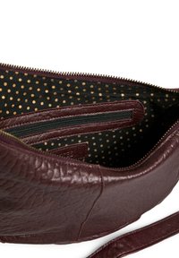 Sac à main en cuir bordeaux avec une finition texturée. L'intérieur est en tissu noir à pois dorés et comporte une poche zippée pour l'organisation.