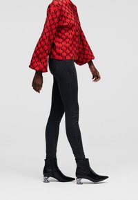 Red jacket with a patterned design, wide sleeves, paired with black textured leggings and pointed-toe ankle boots with block heels.