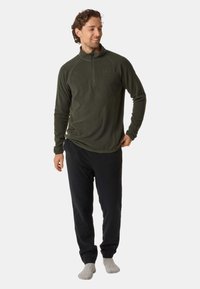 Olivgrön fleece-pullover med halvmåttig krage, kombinerad med svarta byxor. Mjuk textur, åtsittande design, minimal branding på bröstet.