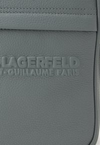 Szürke bőr táska texturált felülettel, kiemelkedő dizájnnal, amelyen a "LAGERFELD ST. GUILLAUME PARIS" márkaneve található, dombornyomott formában.