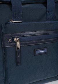 Borsa per laptop in nylon nero con accenti blu scuro, dotata di una tasca frontale con zip, tessuto testurizzato e logo di marca esagonale.