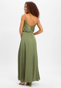 Robe en satin vert olive longue avec des fines bretelles, un dos nu et une jupe fluide. Caractéristiques d'une taille ajustée et d'une fermeture à glissière dans le dos.