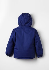 Námořnická modrá nepromokavá bunda s kapucí, vybavená elastickými manžetami a rovnými lemy. Hladká textura s jednoduchým, funkčním designem.
