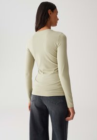 Langarmtop in lichtgroen, aansluitende stijl, met een gladde textuur. Draag het met donkergrijze wijde jeans, voorzien van achterzakken en subtiele naden.