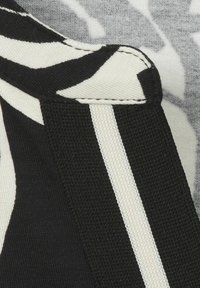 Schwarz-weiß gemusteter Stoff mit strukturiertem Finish. Besitzt einen schwarzen Riemen mit einem weißen Streifen und sichtbarem Nahtdetail.