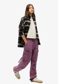 Pantalon cargobroek in paarse katoen met zijzakken, gecombineerd met een wit T-shirt en een zwart geruit flanellen overhemd, gestyled met sneakers.